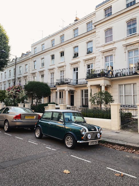 The image shows a quiet residential street with white, multi-storey terraced houses featuring black wrought iron balconies and decorative columns along the facades, typical of Belgravia. Large, mature